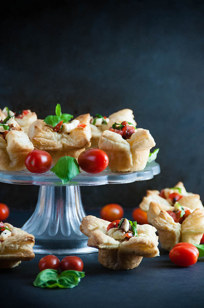 puff pastry cups filled with caprese salad on a clear platter with tomatoes and basil garnish
