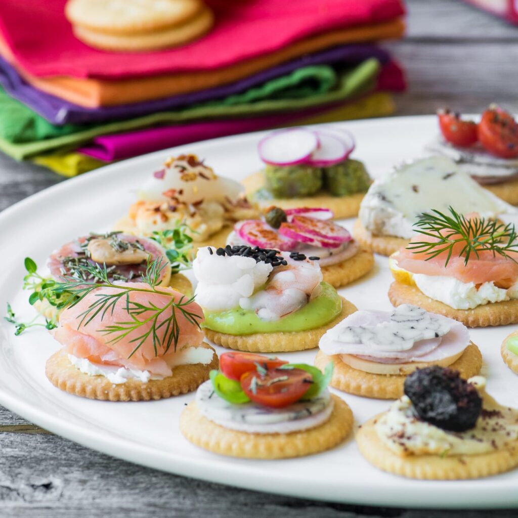 a colorful spread of crackers topped with different spreads and veggies on a white plate