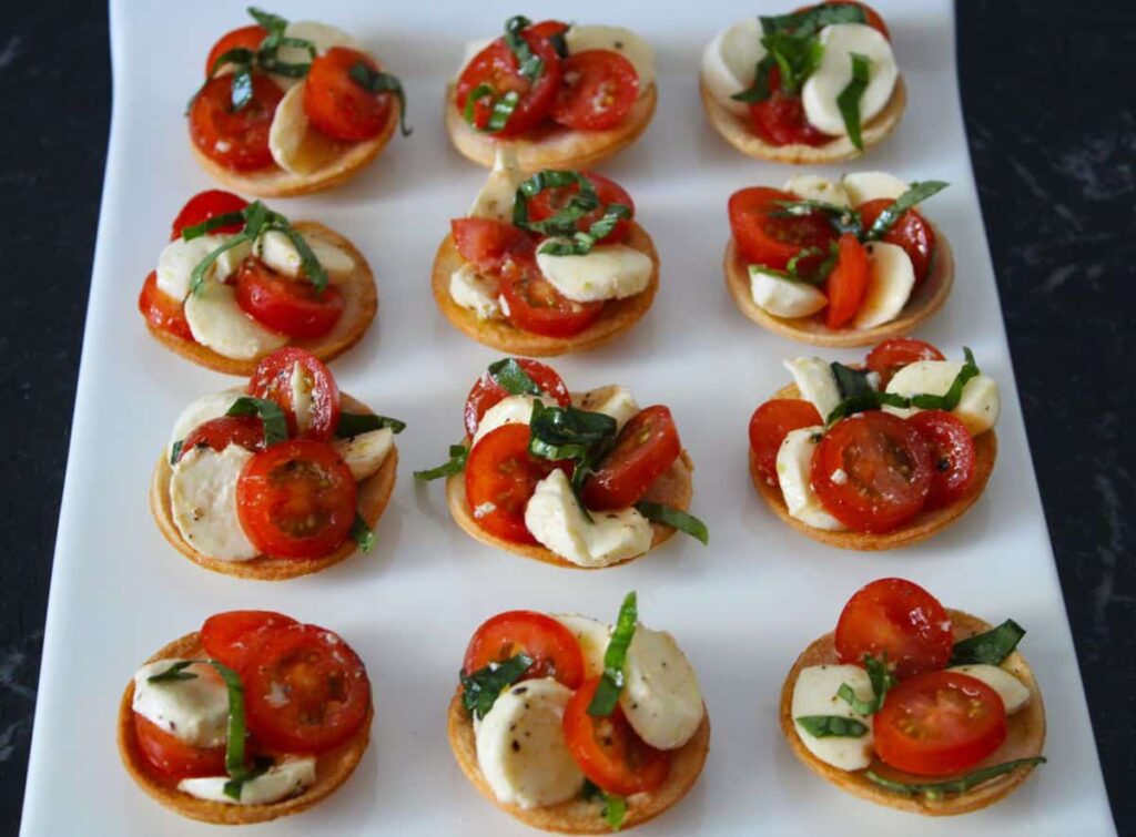 caprese salad over top of crunchy bread rounds on a white serving platter