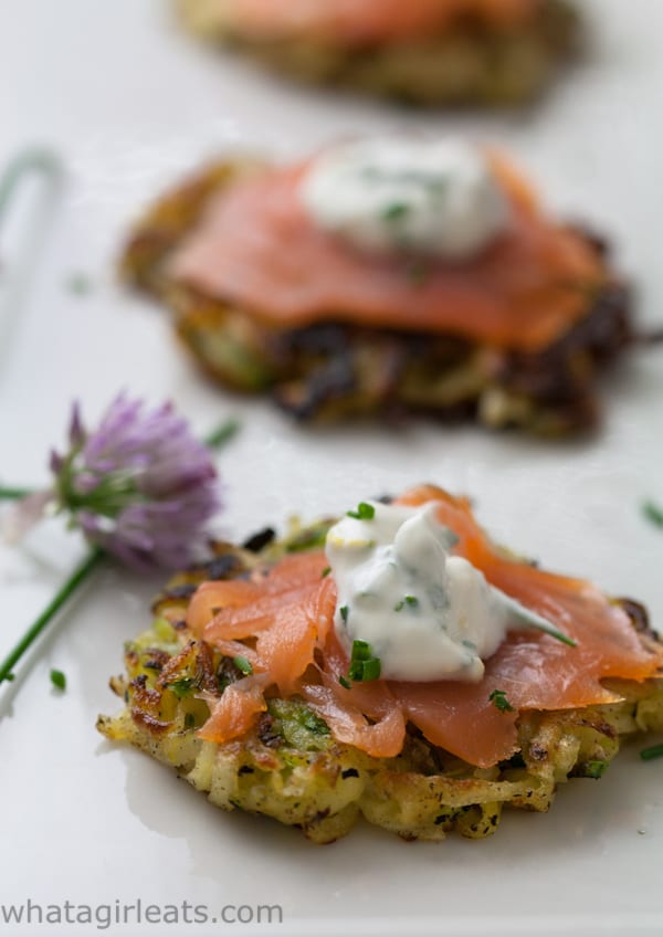 vegetable potato pancakes on a white plate topped with slices of salmon and a dollop of sour cream