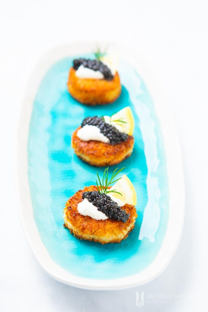 mini salmon bites topped with caviar and sour cream on a long blue plate