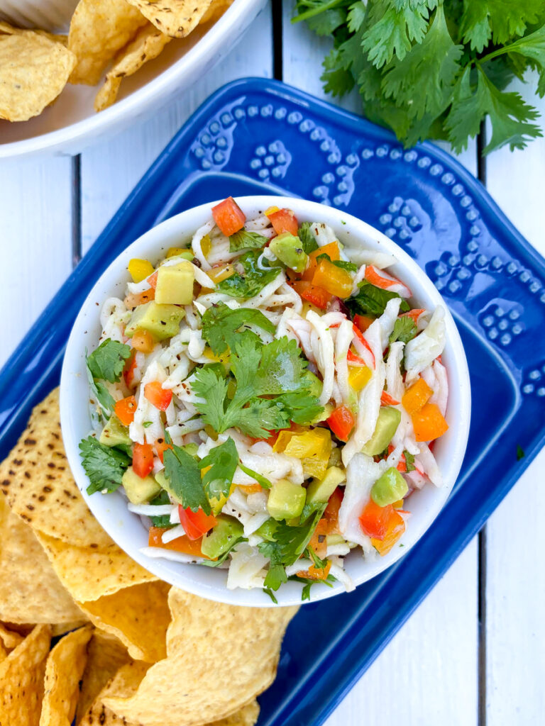 overhead shot of crab ceviche in a white bowl on a blue plate with tostitos