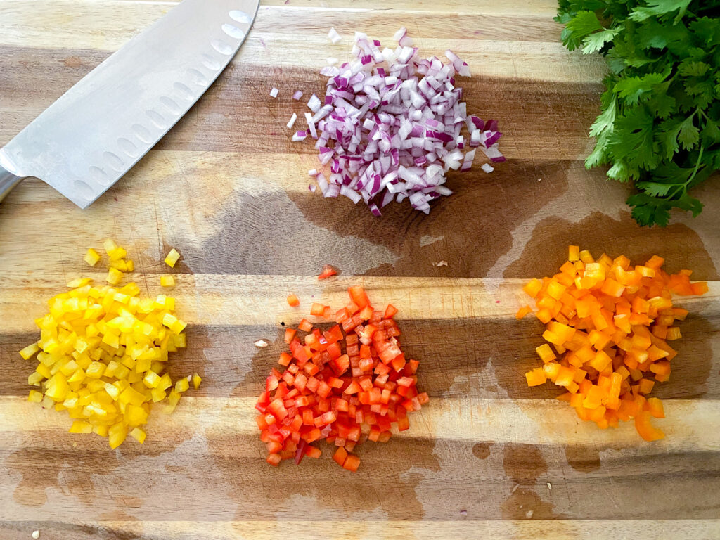 minced red yellow orange bell peppers with red onion on cutting board
