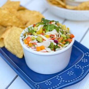 crab meat with peppers and onions in a white bowl with tortilla chips
